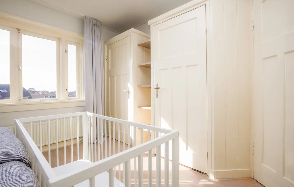 Un cuarto infantil luminoso con una cuna blanca junto a una ventana.