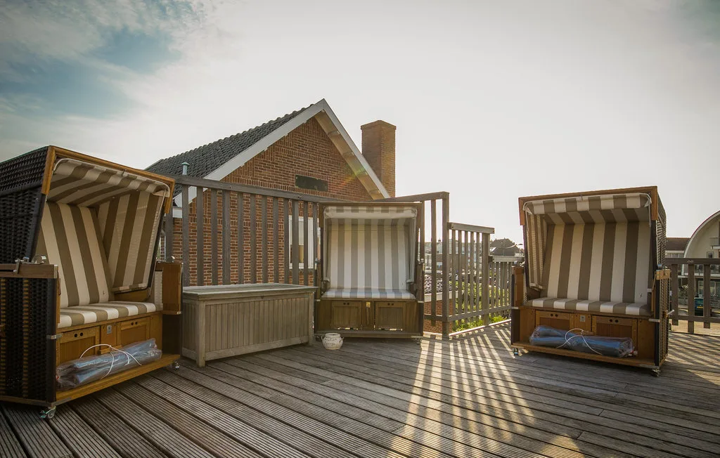Una terraza de madera tiene asientos exteriores a rayas y una barandilla bajo el sol.