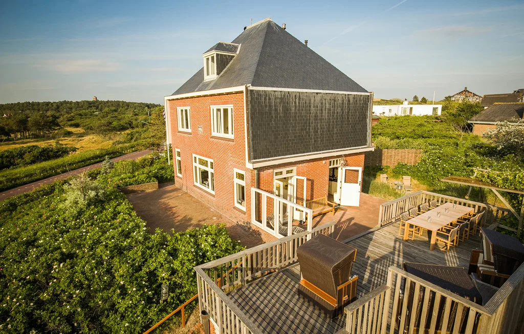 Una casa de ladrillo rojo con una amplia terraza de madera y asientos al aire libre.