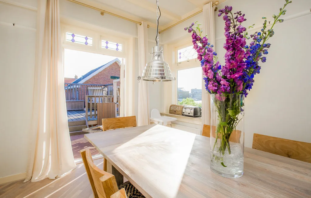 Un comedor luminoso con una mesa de madera y flores coloridas en un jarrón de vidrio.
