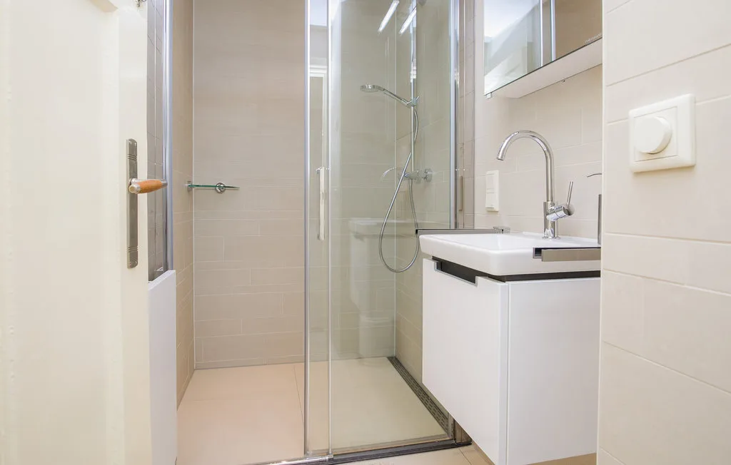 Un baño moderno con una ducha de vidrio y un lavabo blanco.