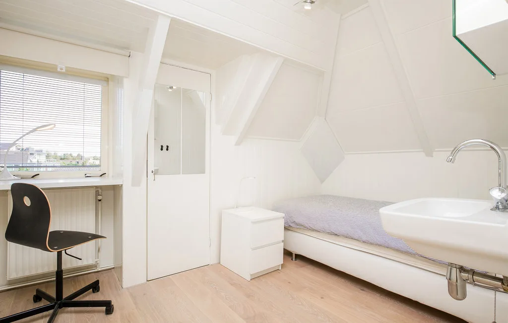 Un dormitorio luminoso con cama, escritorio y lavabo bajo un techo inclinado.