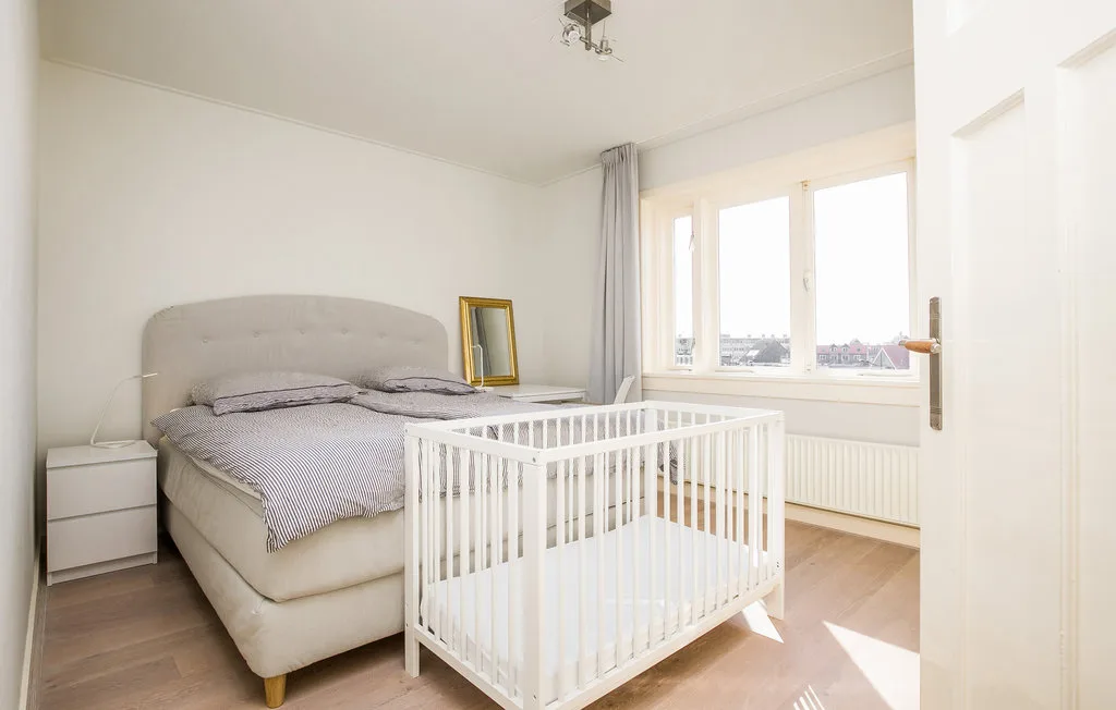 Un dormitorio luminoso con una cama y una cuna blanca junto a la ventana.
