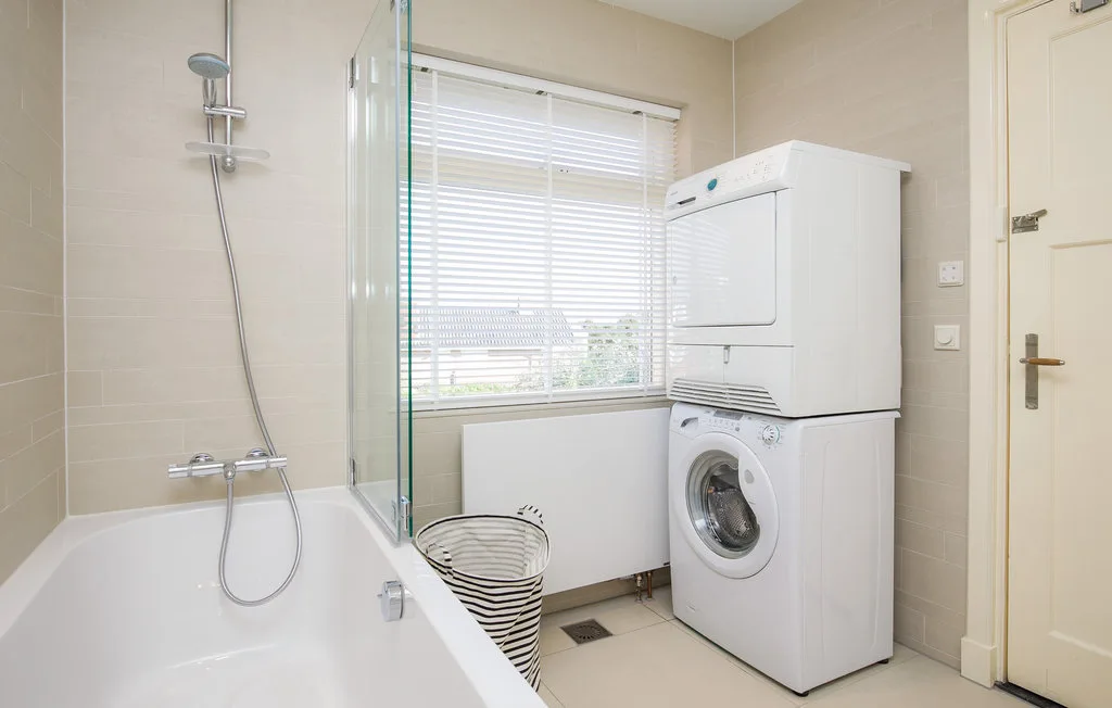 Un baño luminoso con bañera, ducha y lavadoras apiladas.