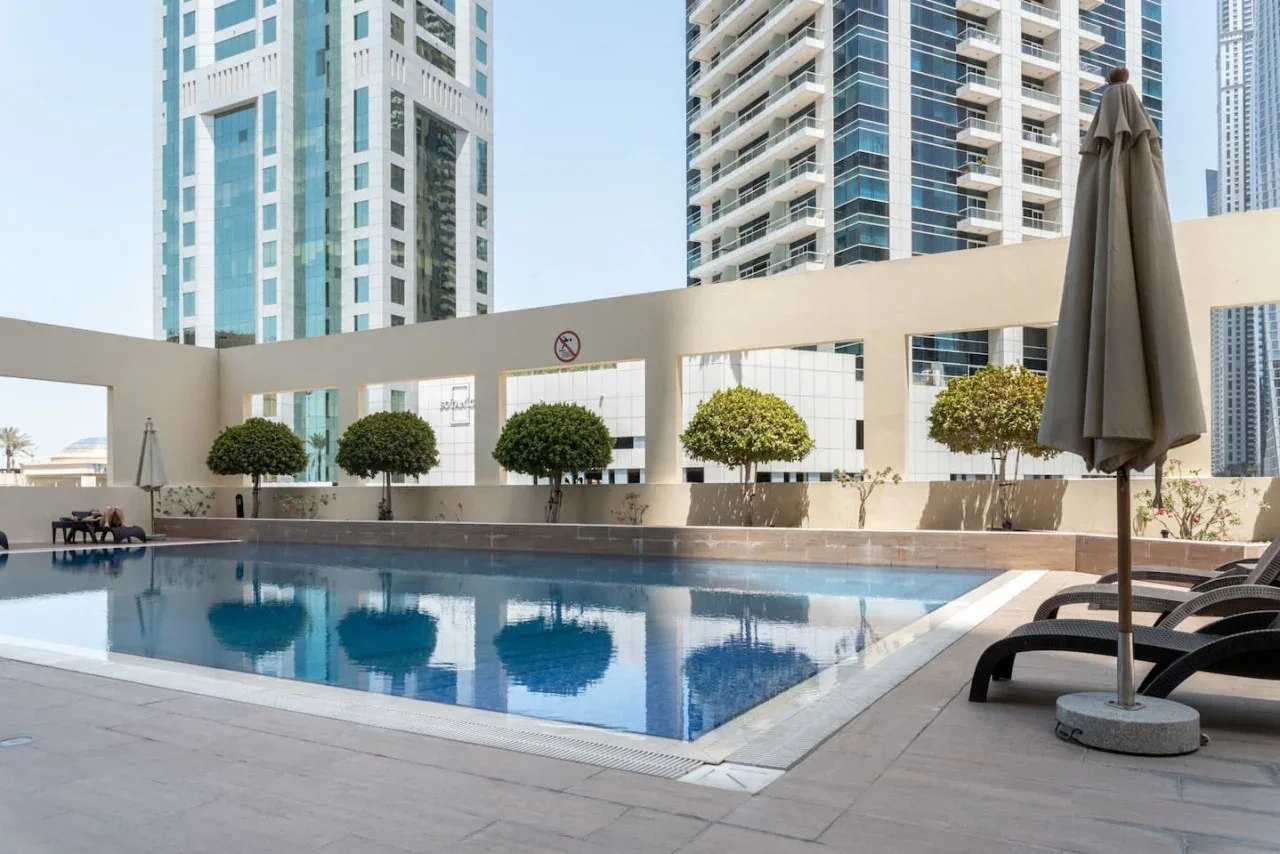 Una piscina en la azotea con asientos y edificios altos al fondo.