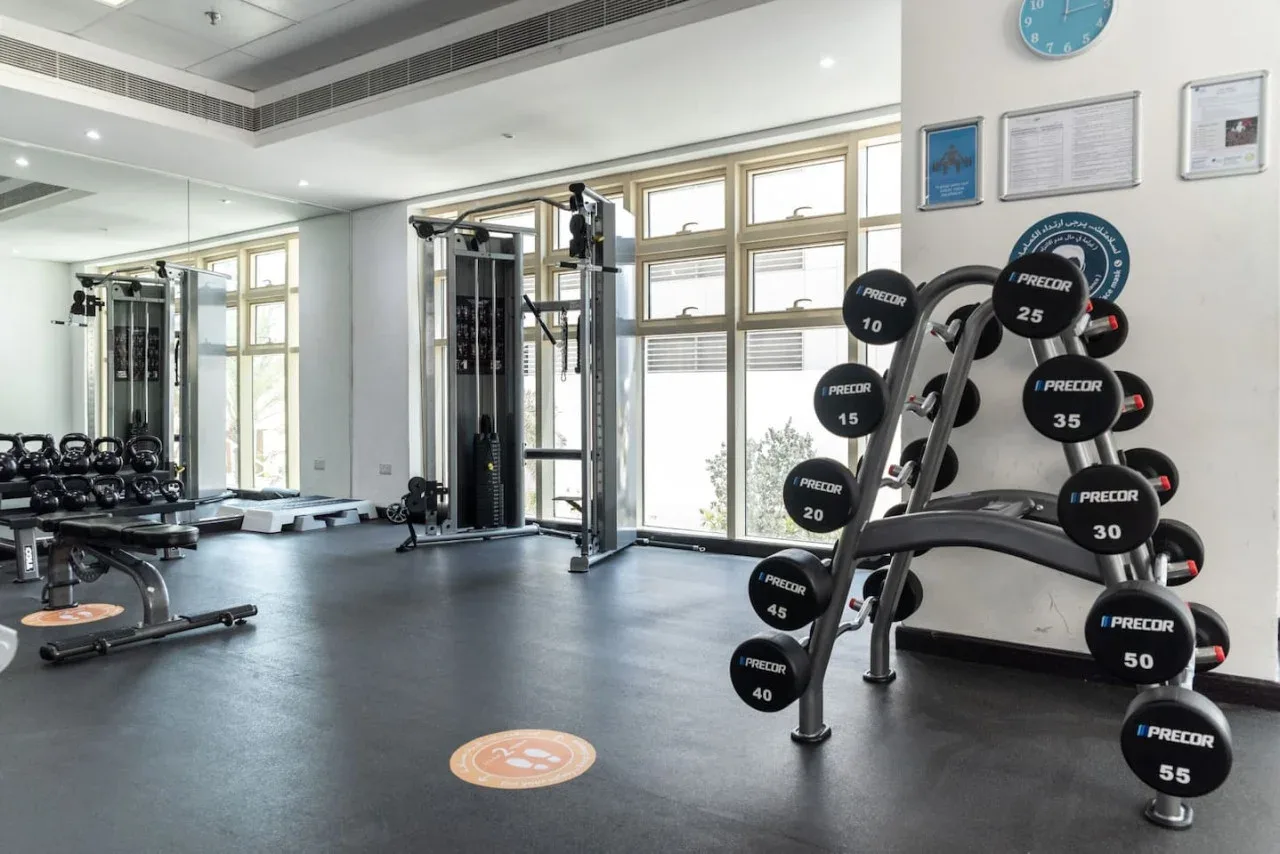 Un gimnasio con pesas y equipo de ejercicio junto a grandes ventanas.