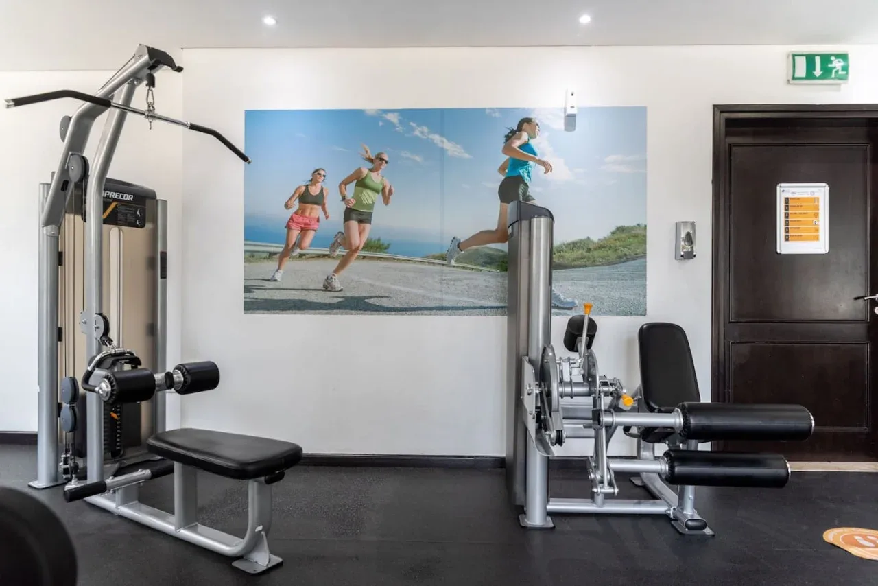 Un gimnasio con máquinas de pesas y un gran mural de corredores en la pared.