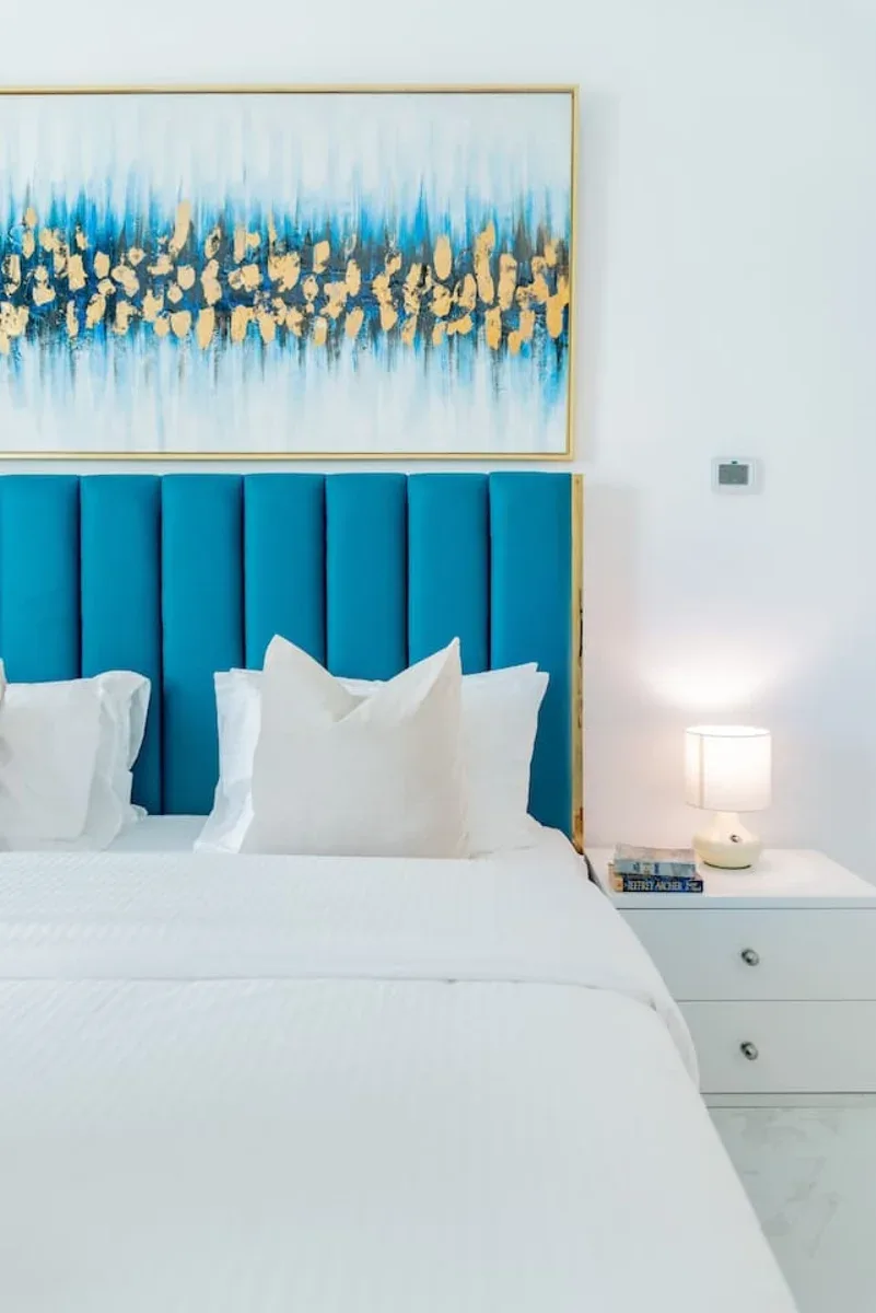 Una cama bien tendida con ropa de cama blanca y un cabecero tapizado azul.