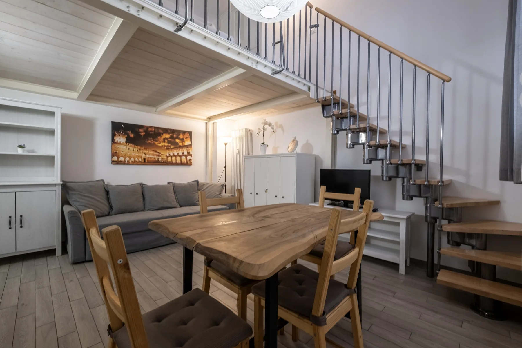 A dining area with a wooden table and chairs beneath an open staircase.