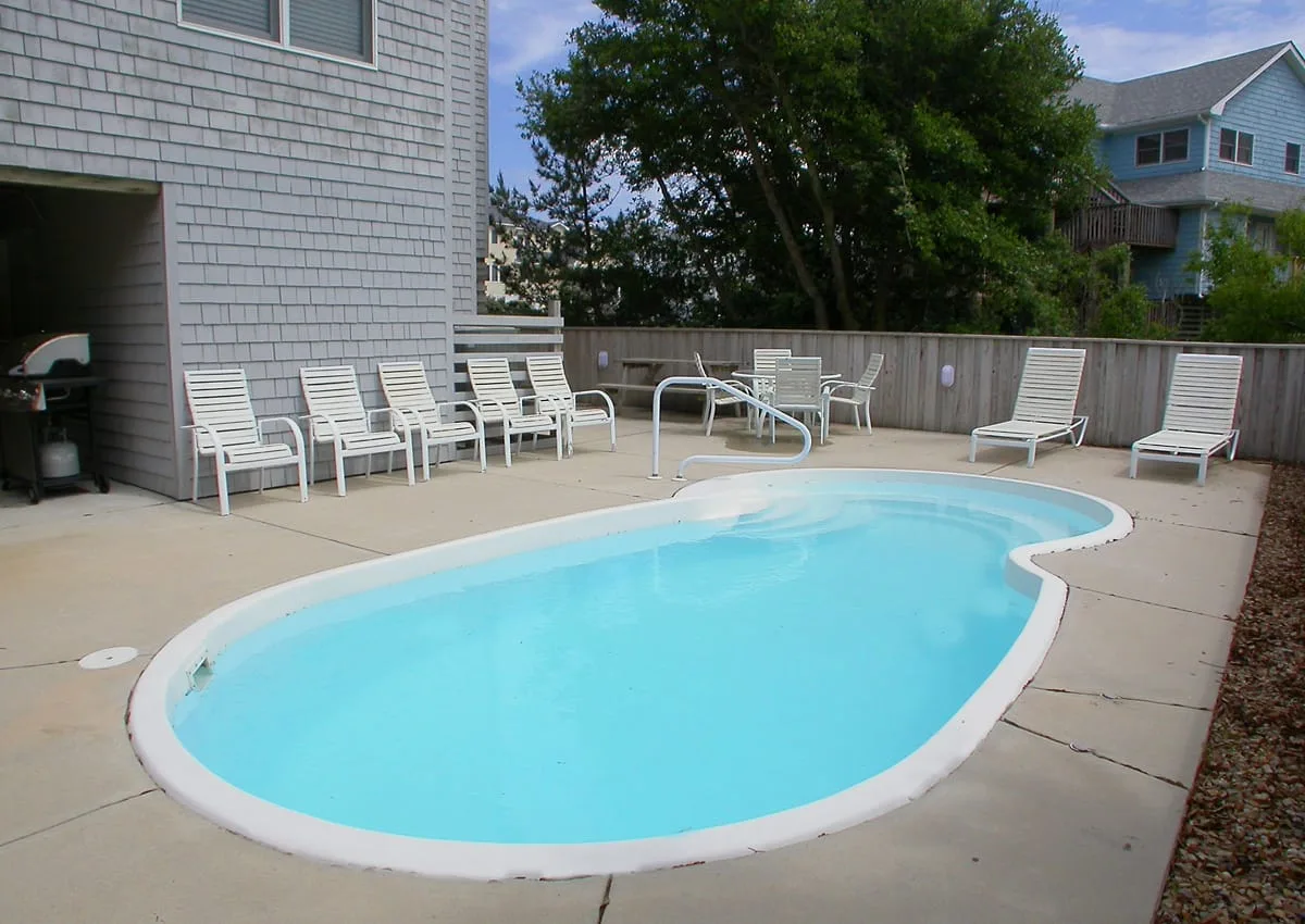 An outdoor swimming pool sits beside a paved deck with seating.