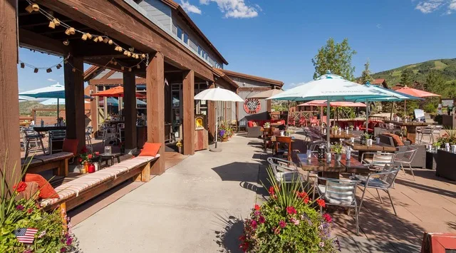 Un patio de restaurante al aire libre tiene mesas y asientos bajo sombrillas grandes.