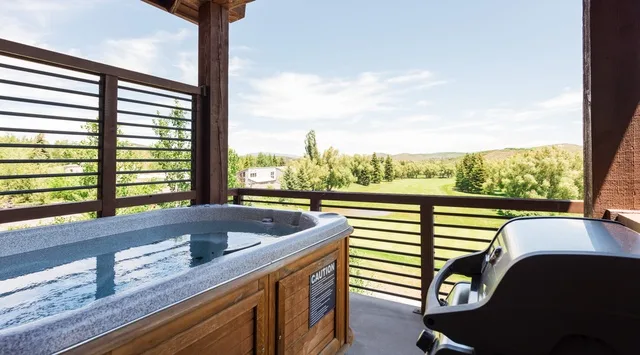 Una bañera de hidromasaje al aire libre está en una terraza con vistas a un paisaje verde.