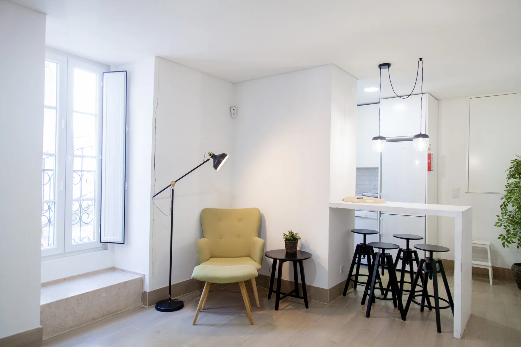 Bright apartment interior with a yellow armchair and a kitchen counter with stools.