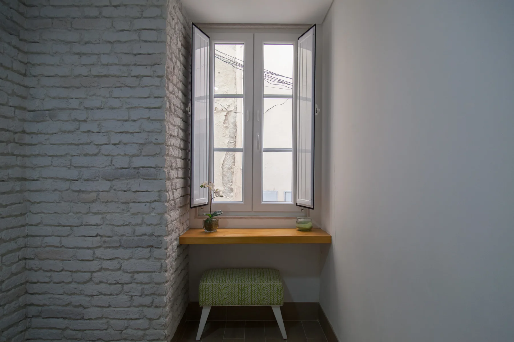 A narrow interior nook with a tall window, wooden sill, and small green seat.