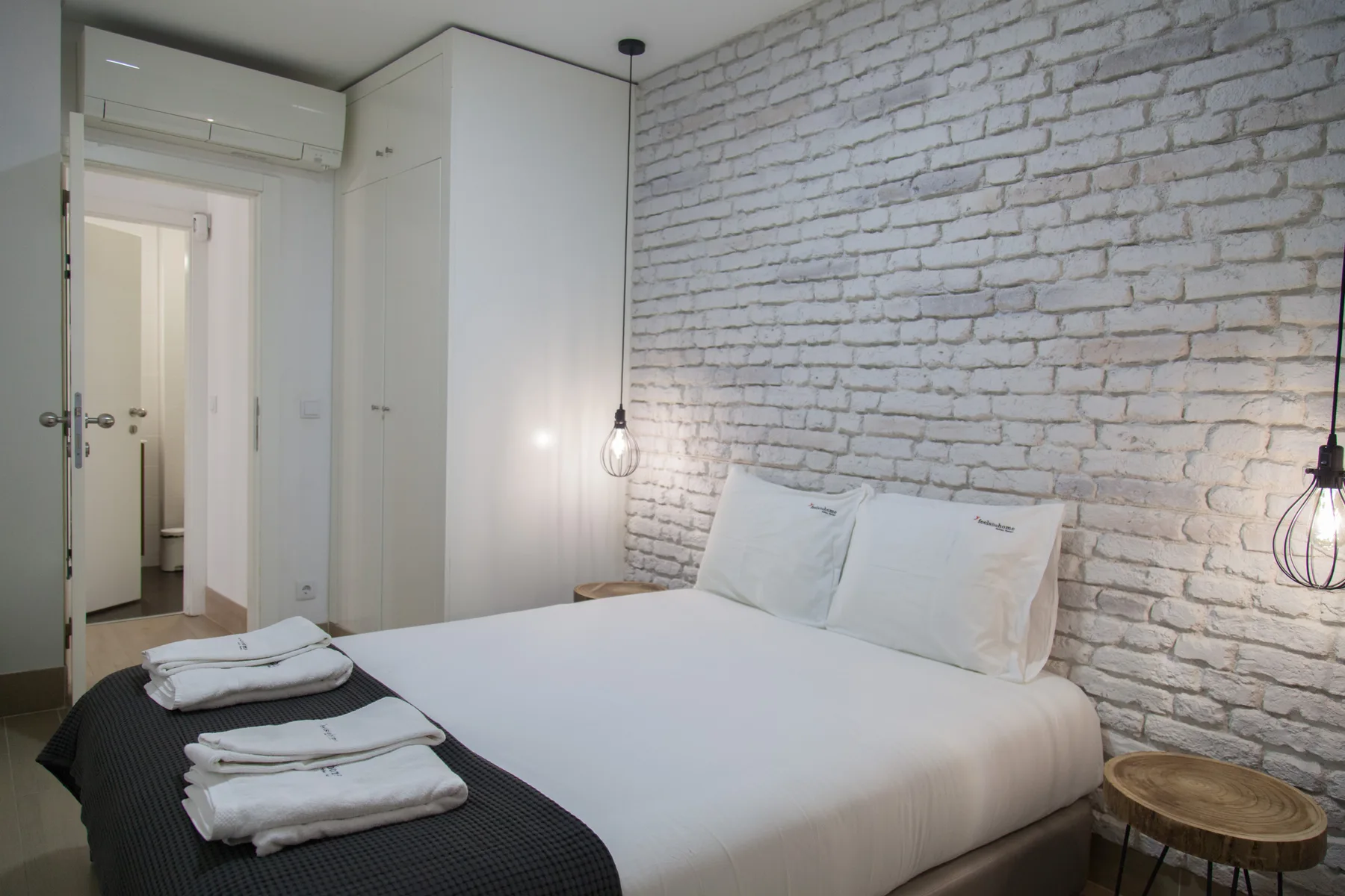 A bedroom with a neatly made bed against a white brick wall.
