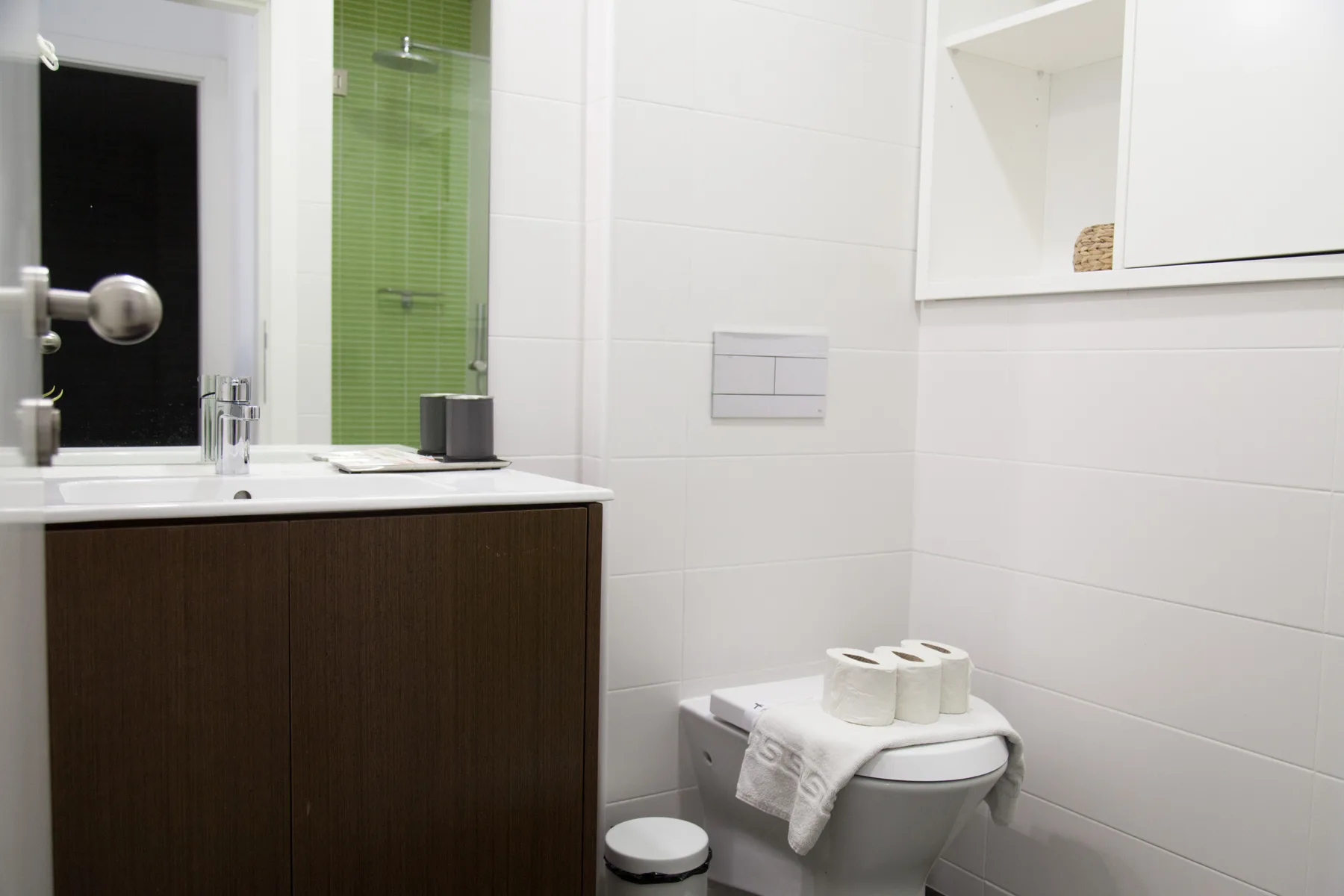 A bathroom with a vanity, toilet, and green-tiled shower area.