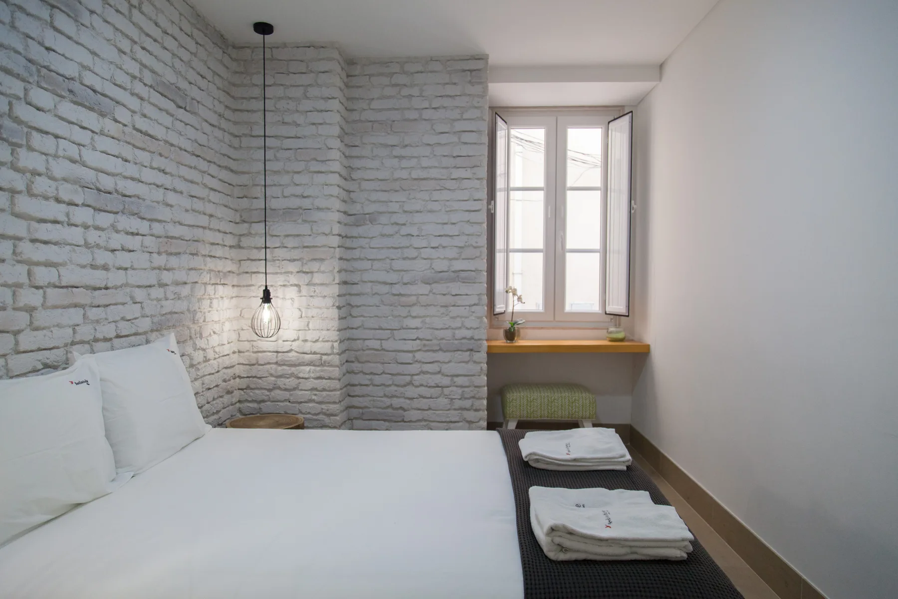 A bedroom with a bed beside a white brick wall and a window.