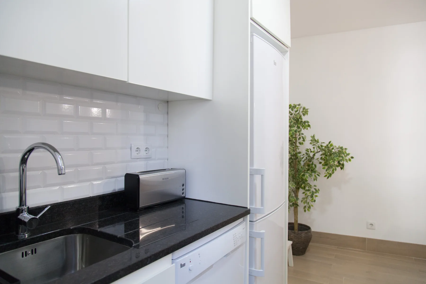 A bright kitchen with a dark countertop and white tile backsplash.
