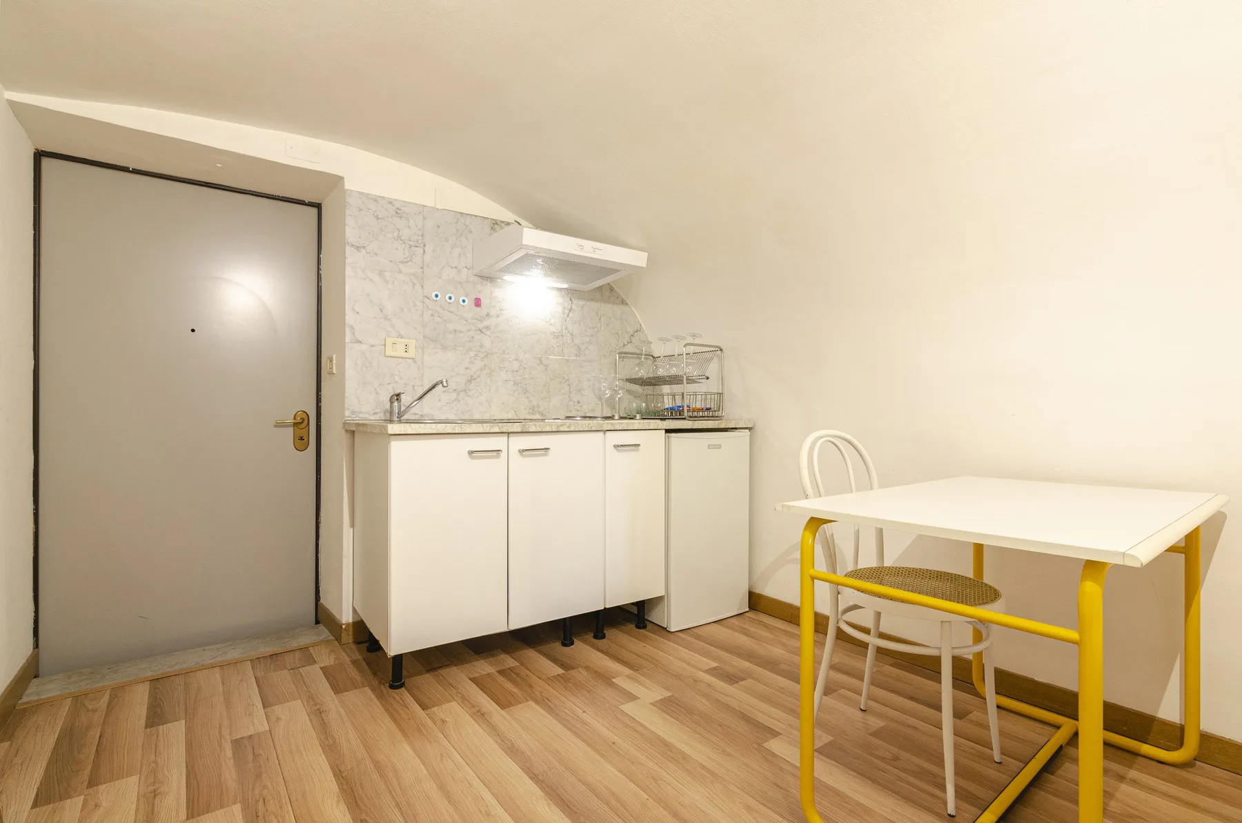 Una cocina pequeña con zona de comedor, armarios blancos y una mesa.