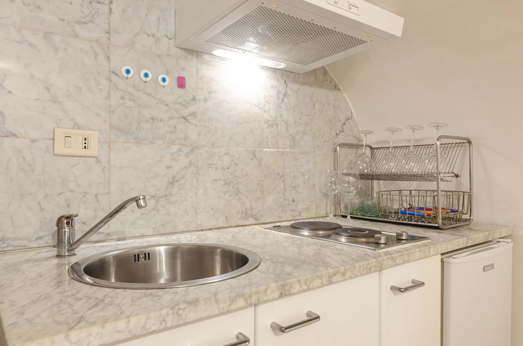 Una encimera de cocina compacta con fregadero de acero inoxidable, placa de cocción y escurridor.