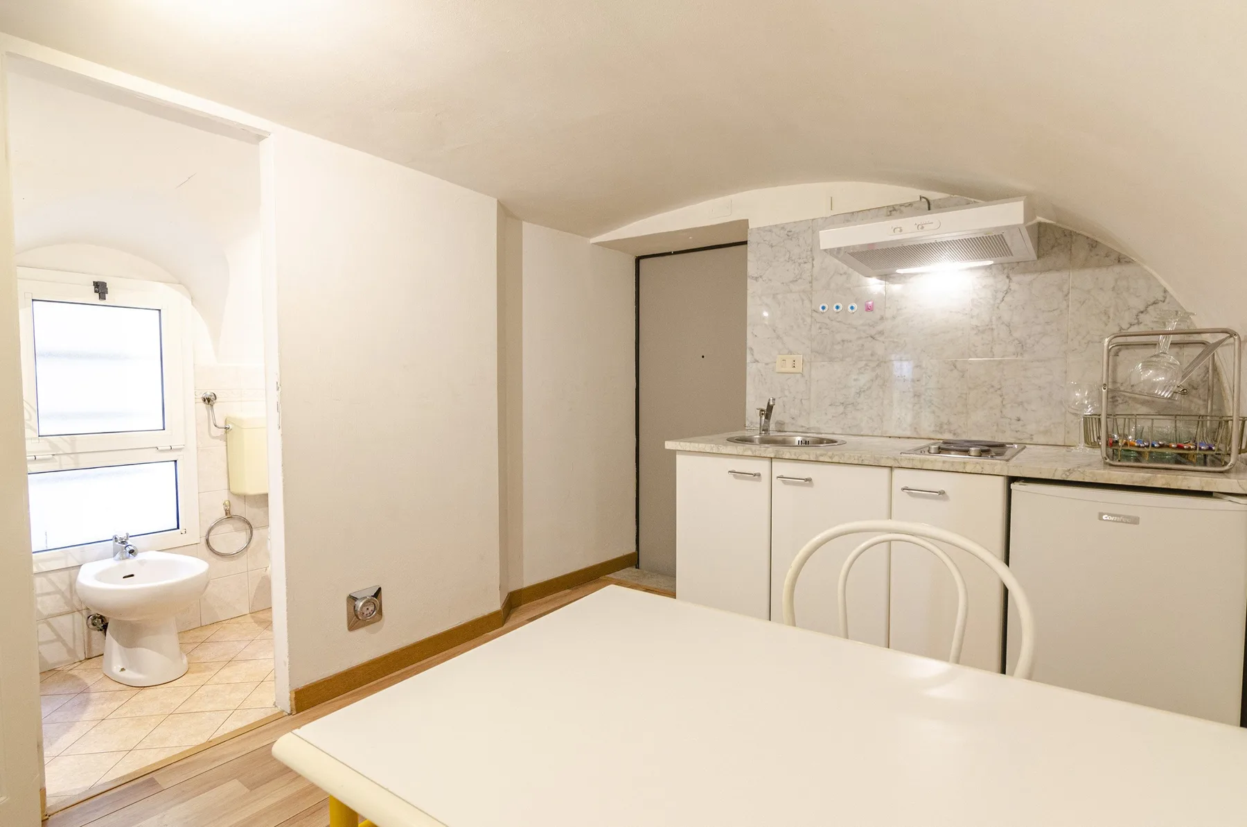 Comedor con mesa y asientos junto a una cocina compacta y un baño.