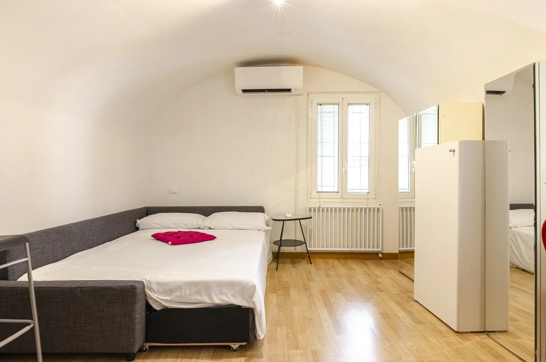 Un dormitorio luminoso con una cama, una mesita y un armario con espejo.
