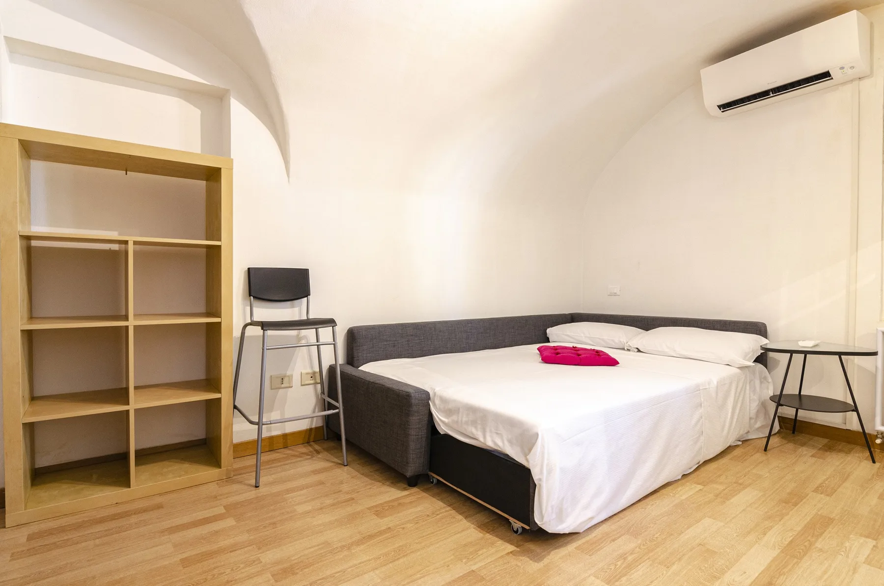 Un dormitorio con una cama, estanterías abiertas y un aire acondicionado de pared.