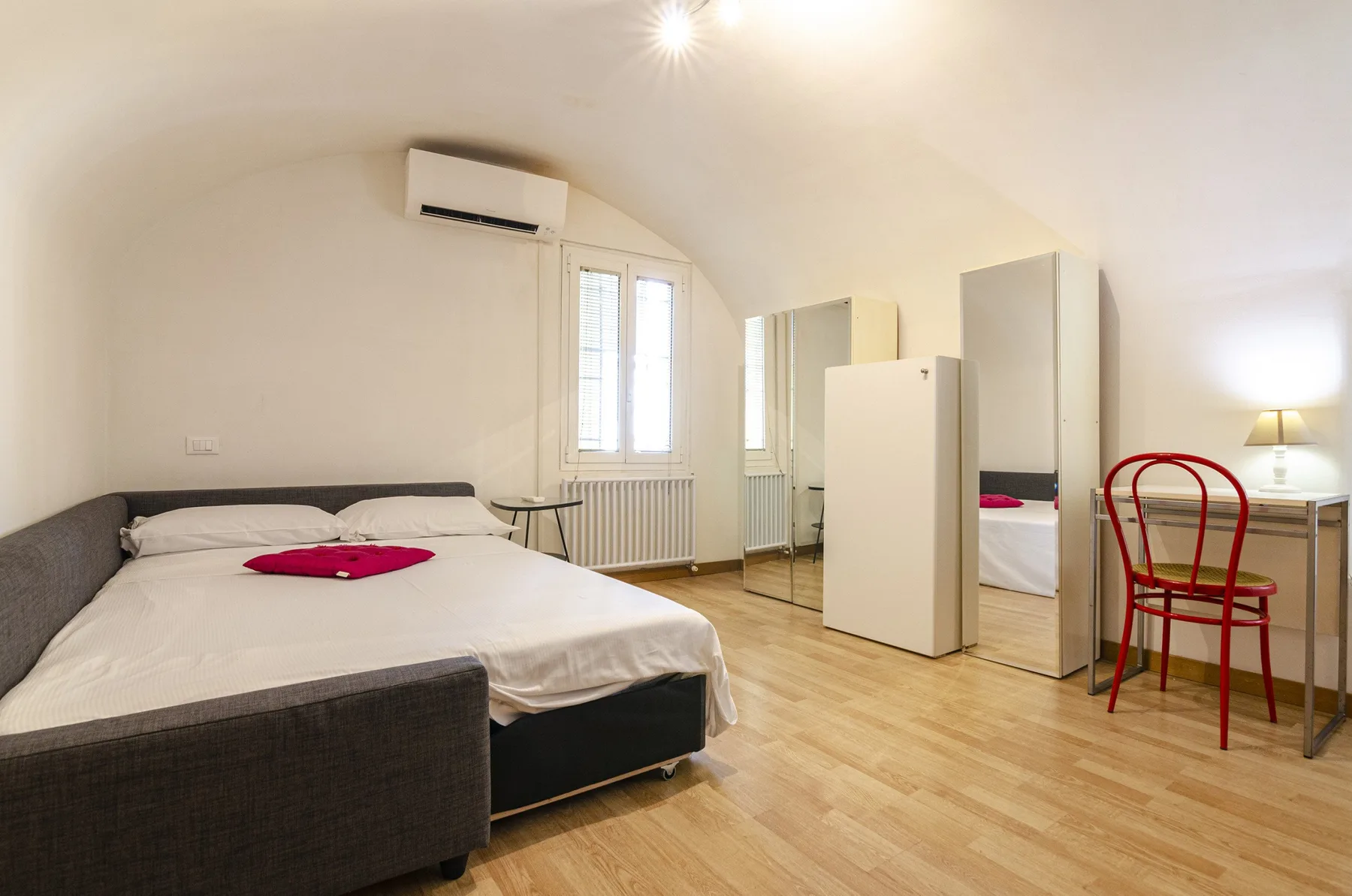 Un dormitorio con una cama, un armario con espejo y una silla roja.