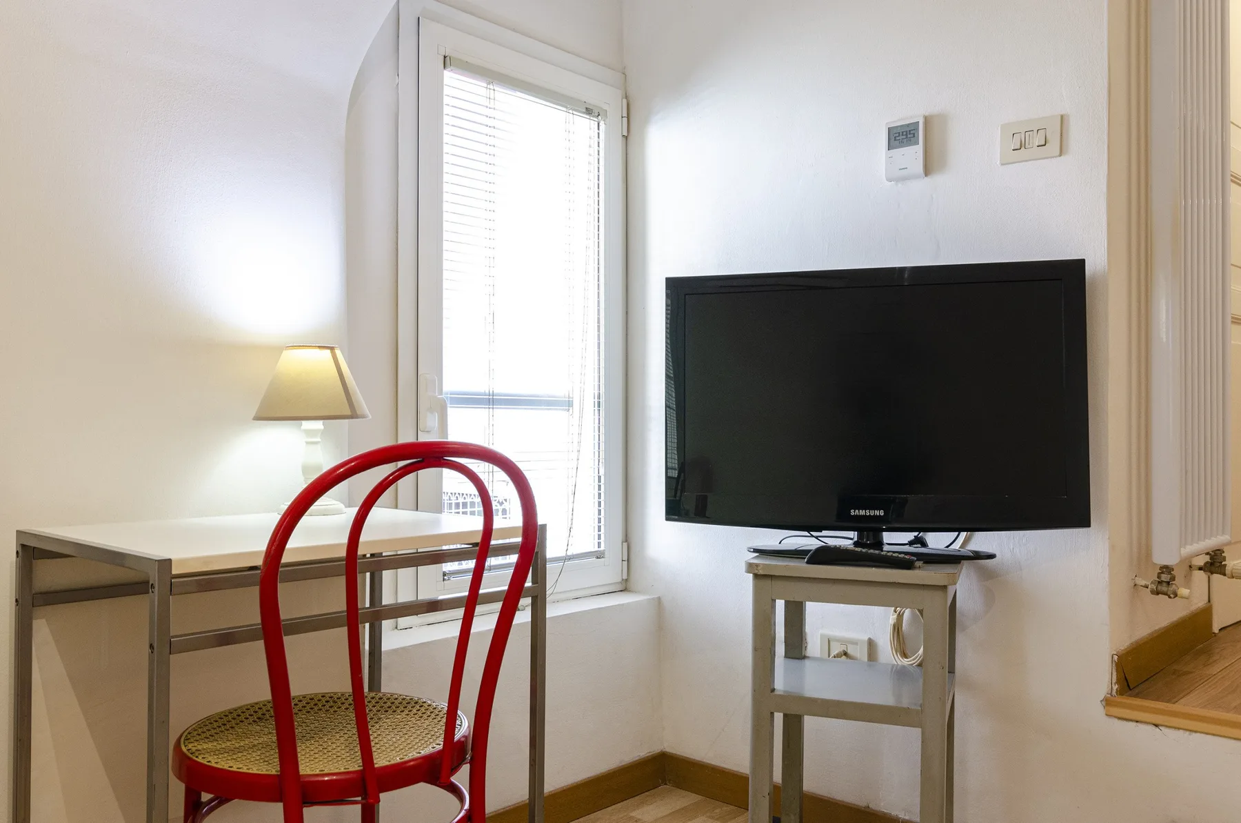 Una habitación luminosa con una mesa, una silla roja y un televisor junto a una ventana.