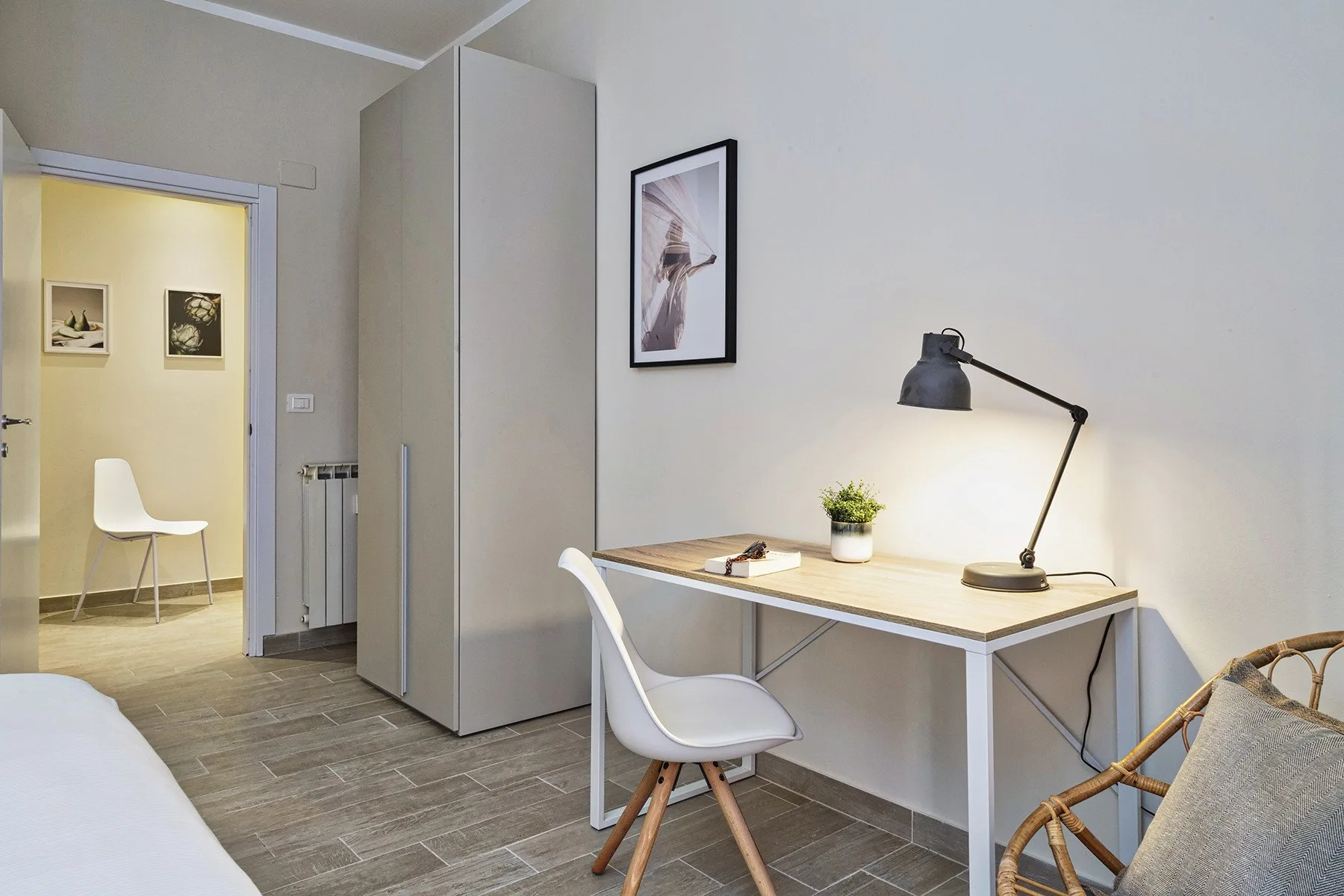 A bedroom workspace with a desk, chair, and lamp beside an open doorway.