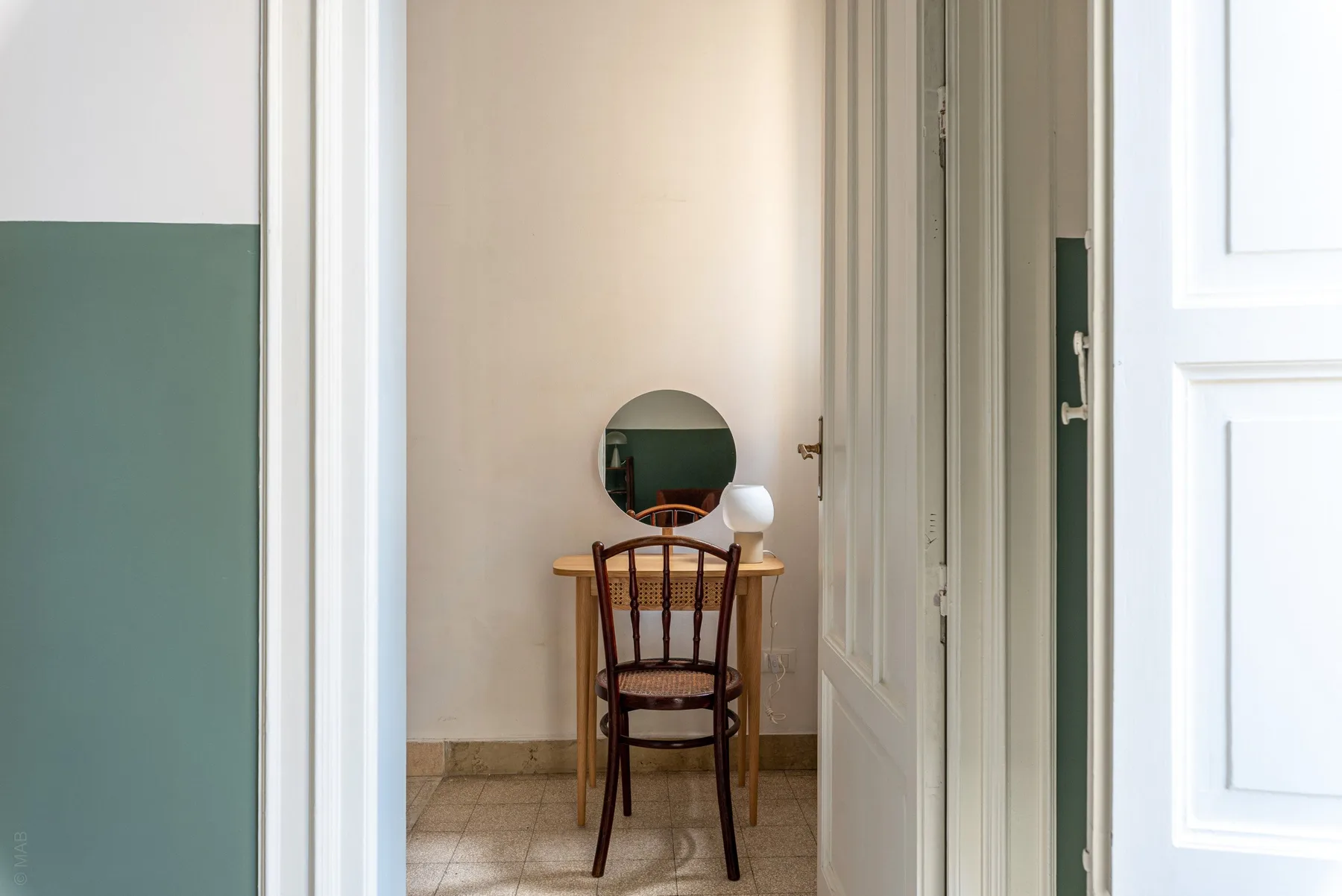 A small entry area with a wooden chair and a round mirror above a narrow table.