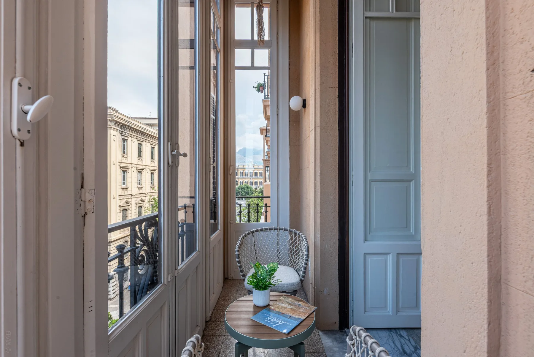 A narrow balcony seating area has a small table and a view of neighboring buildings.