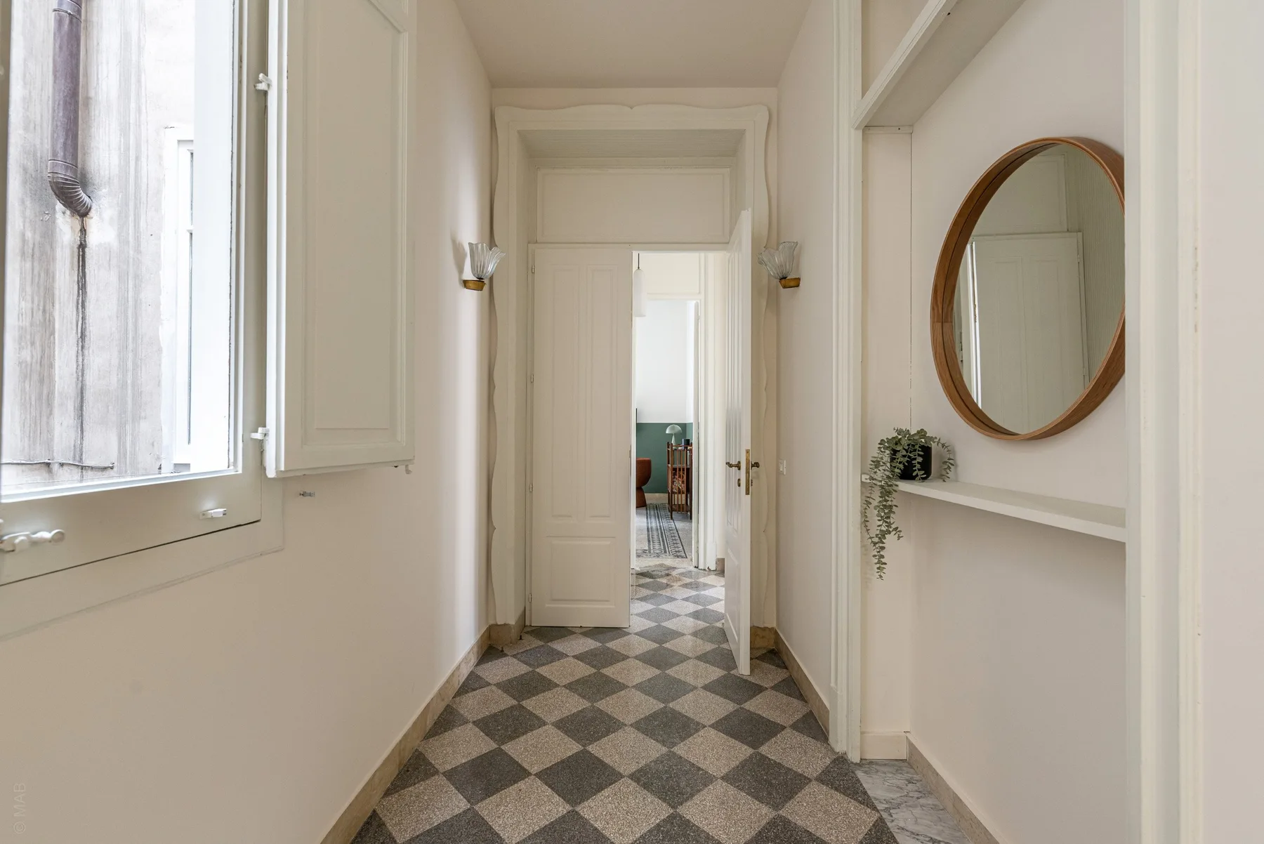 A bright hallway with a checkered floor and an oval mirror.