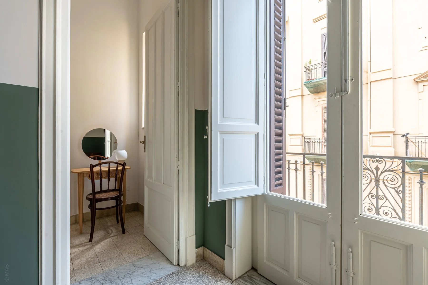 A bright room with a small table and chair beside open balcony doors.
