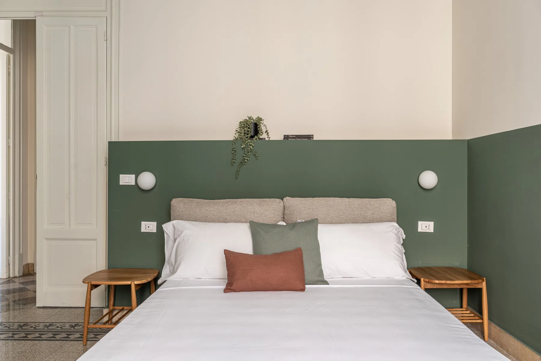 A bedroom with a neatly made bed against a green accent wall.