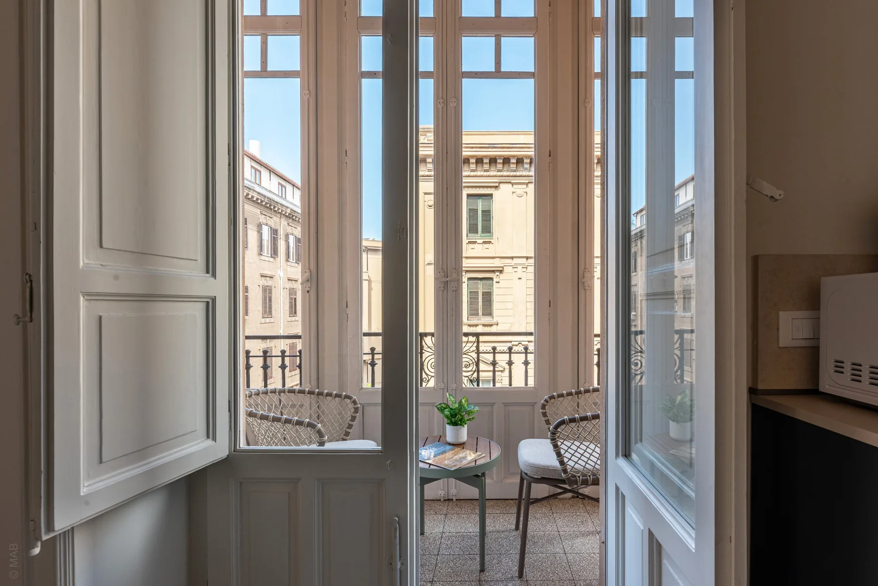 A bright sitting area opens onto a small balcony overlooking nearby buildings.