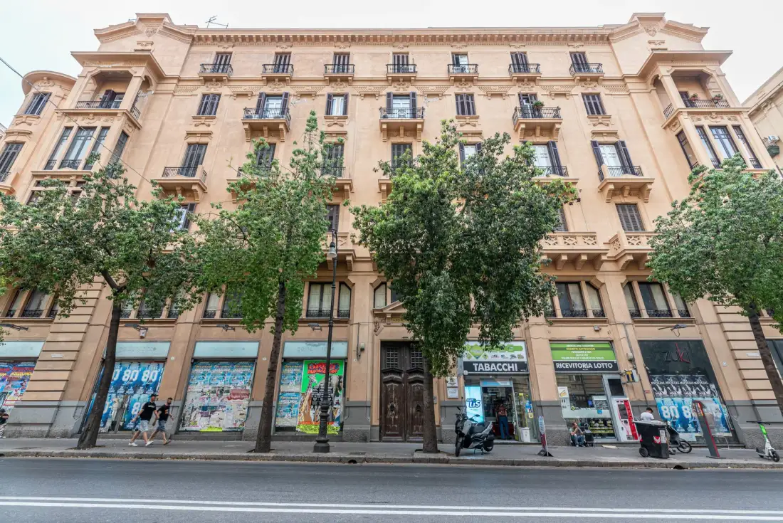 A multi-story stone building with balconies and storefronts along the street.