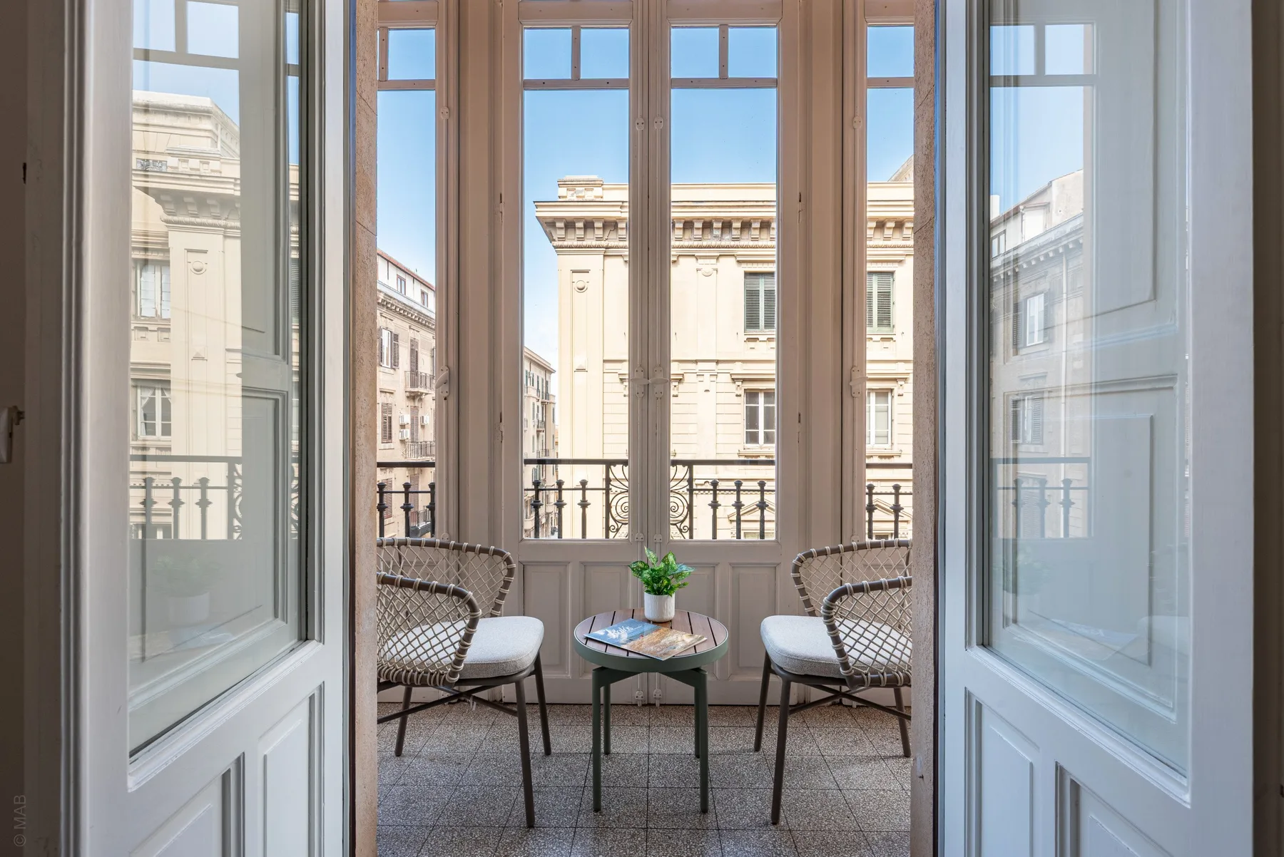 A bright balcony seating area with a small table overlooks neighboring buildings.