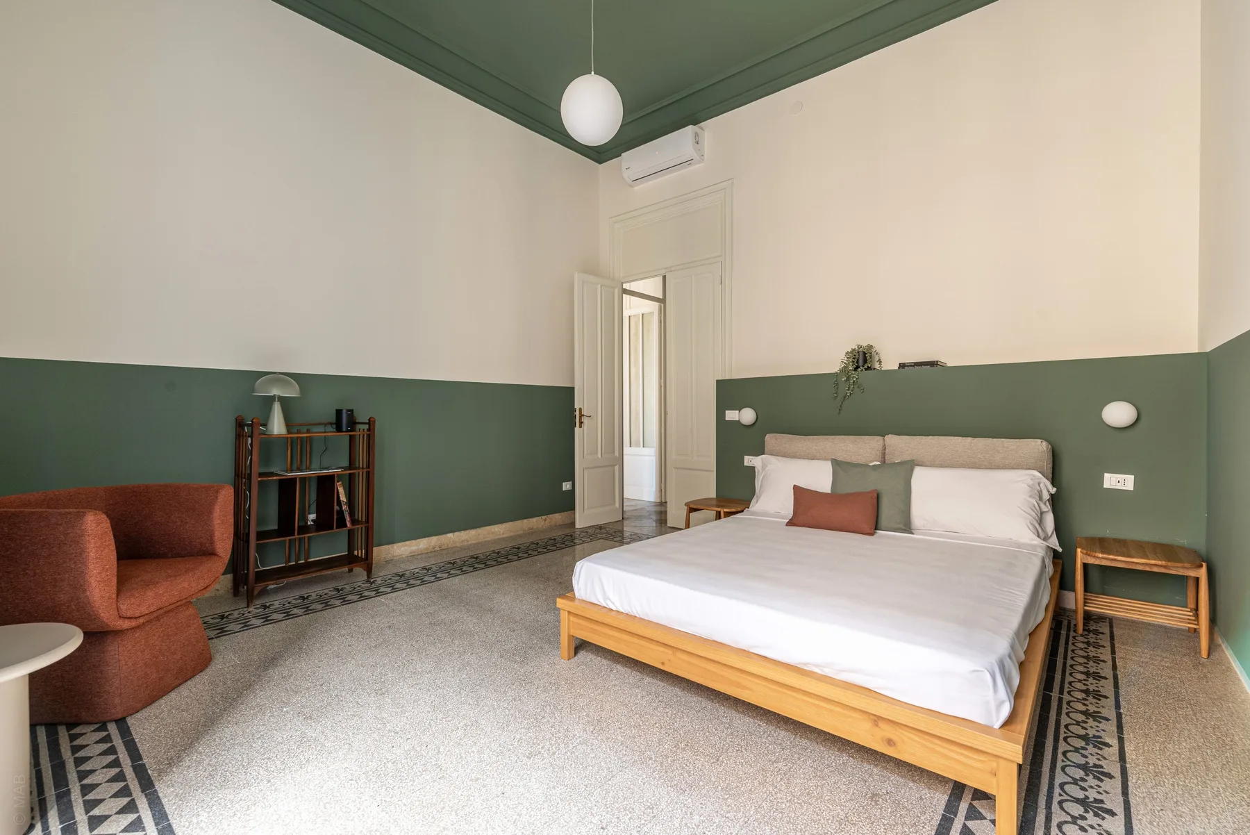 A bedroom with a double bed, green walls, and a rust-colored armchair.