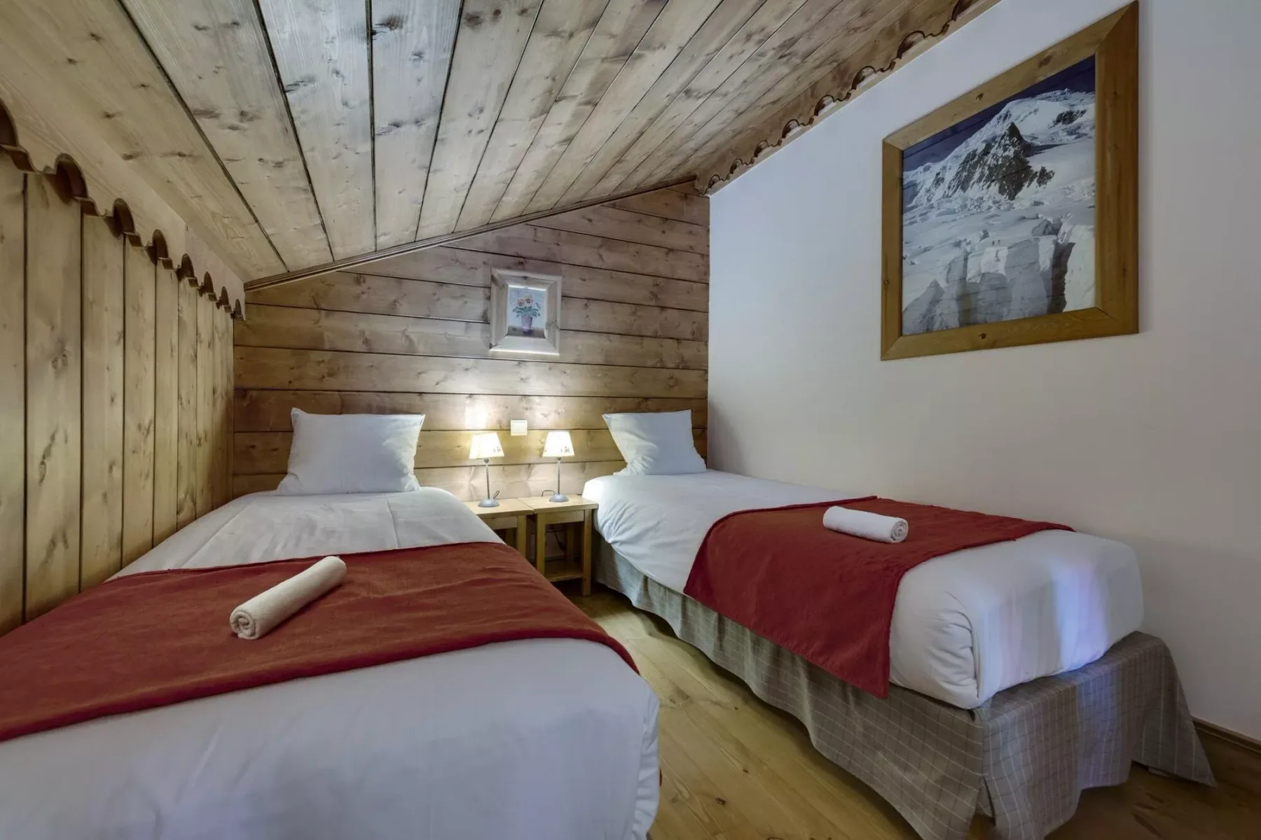 Un dormitorio con dos camas, cubrecamas rojos y paredes revestidas de madera.