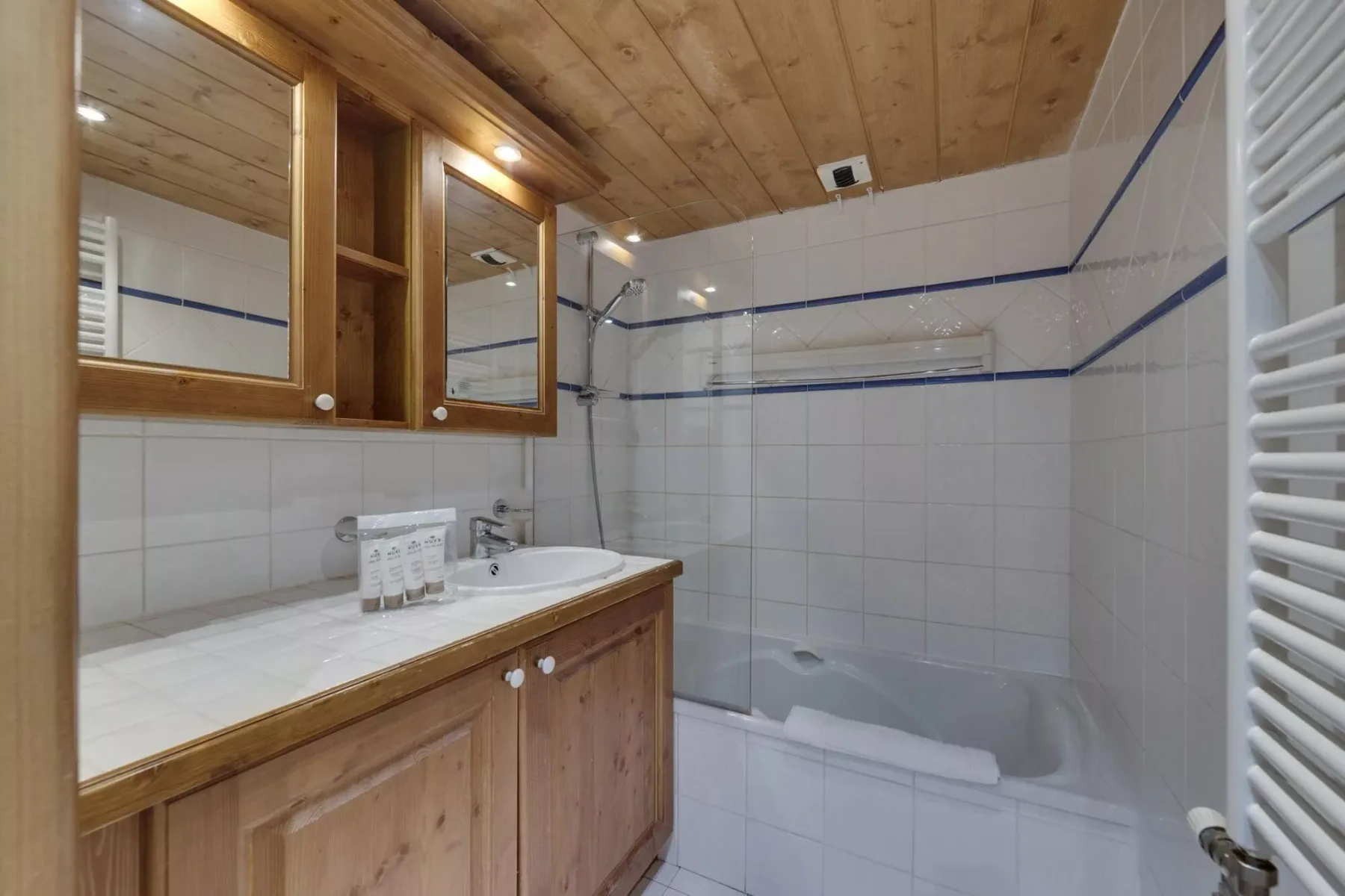 Un baño con azulejos, un tocador de madera, espejos y una bañera con ducha.