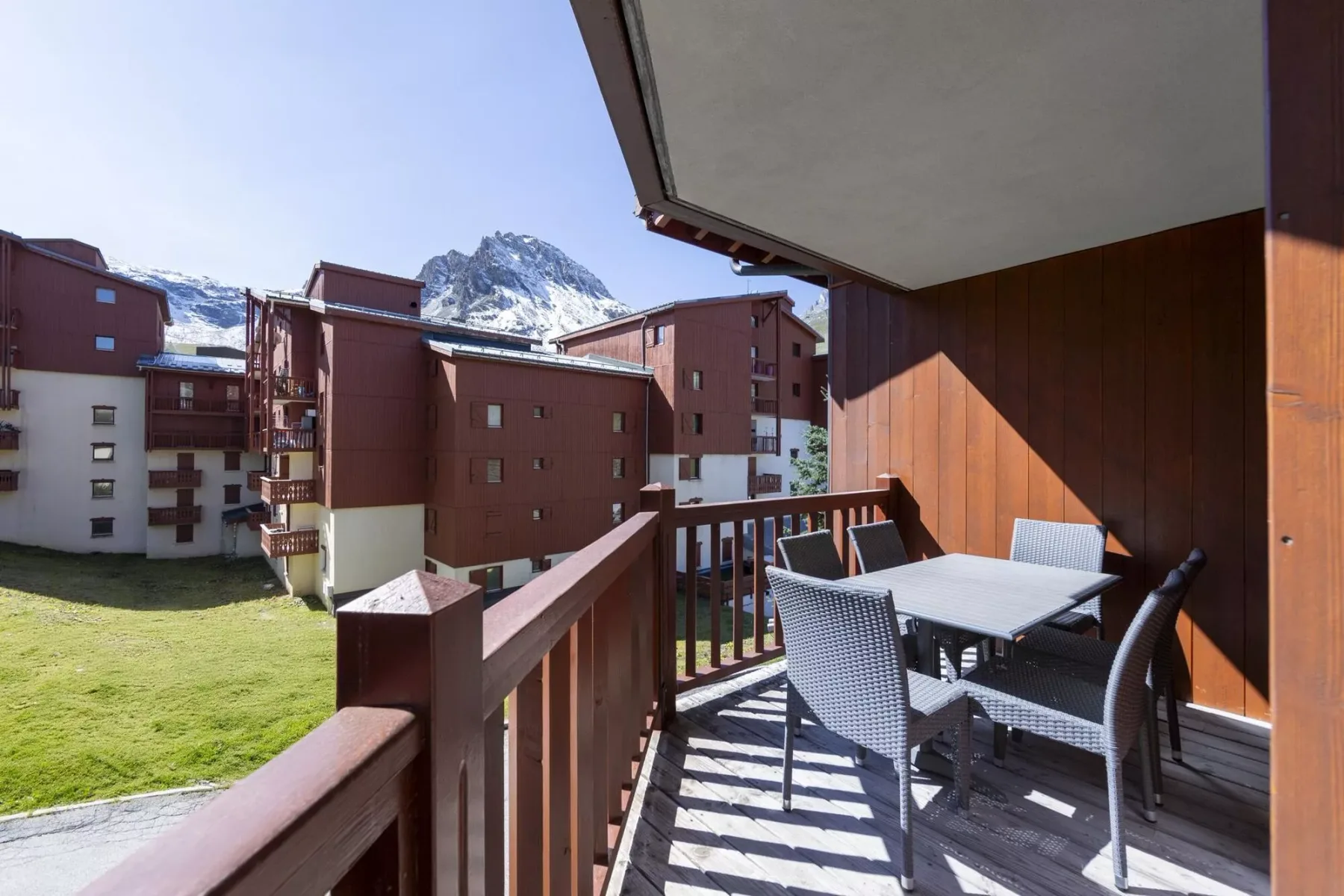 Una zona de comedor en el balcón con asientos exteriores da a edificios cercanos y una montaña.