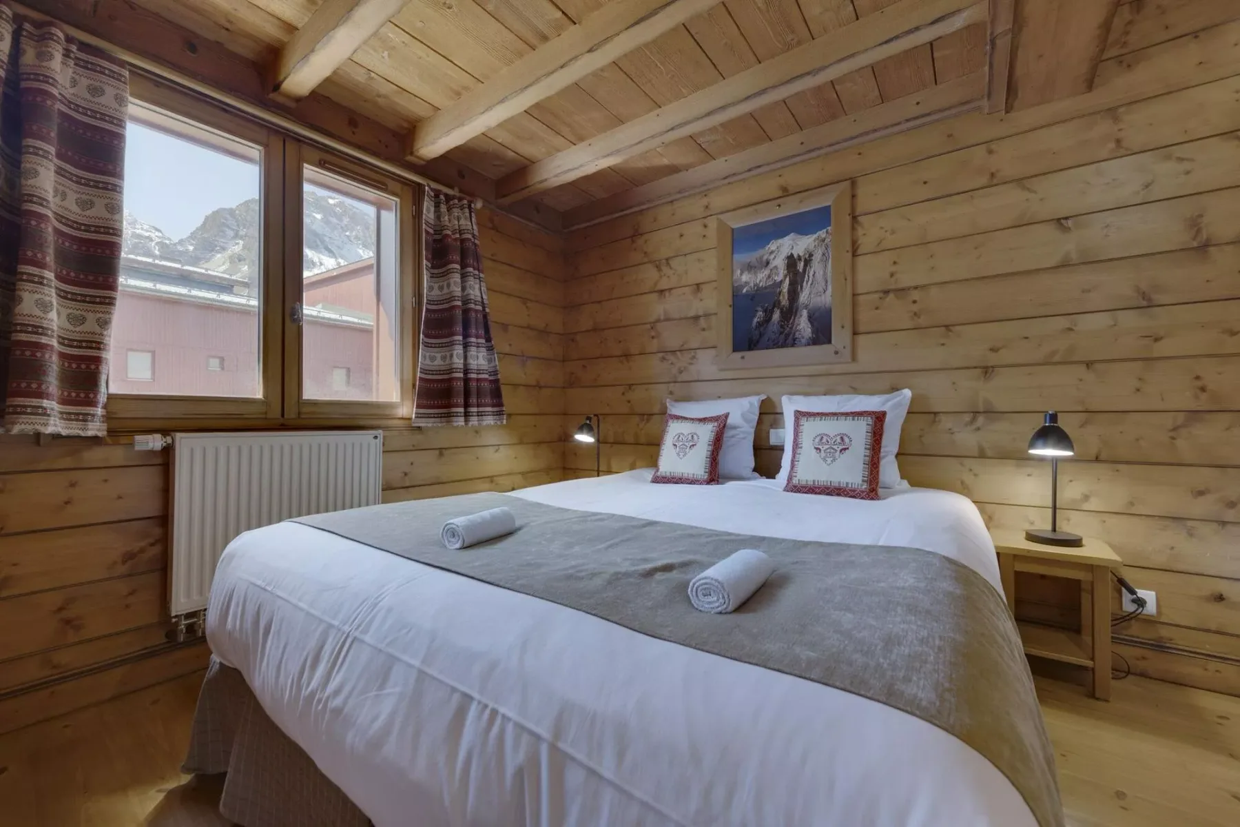 Un dormitorio revestido de madera, con una cama tendida y una ventana con vista a edificios cercanos.