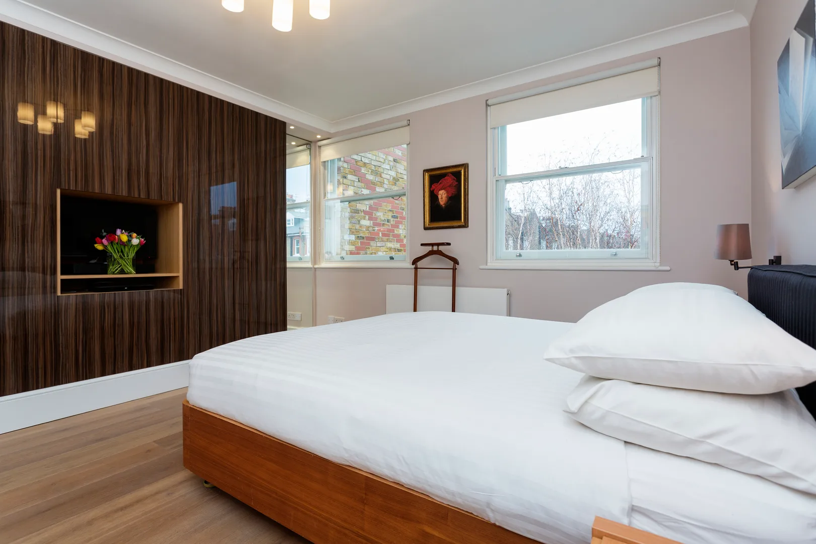 A bedroom with a large bed and windows overlooking neighboring buildings.