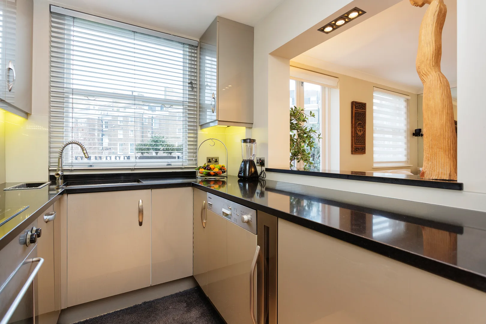 Una cocina moderna con encimeras oscuras y una ventana amplia con vistas a edificios cercanos.