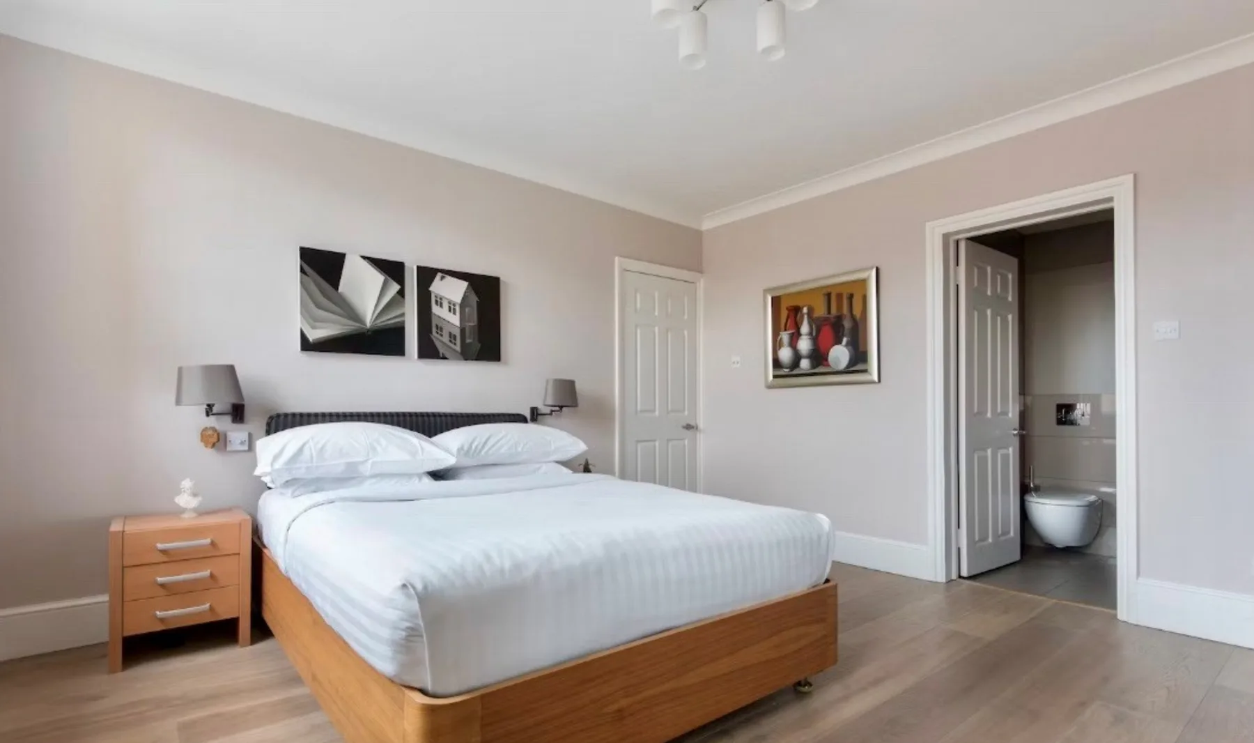 Un dormitorio con una cama tendida y cuadros en las paredes.