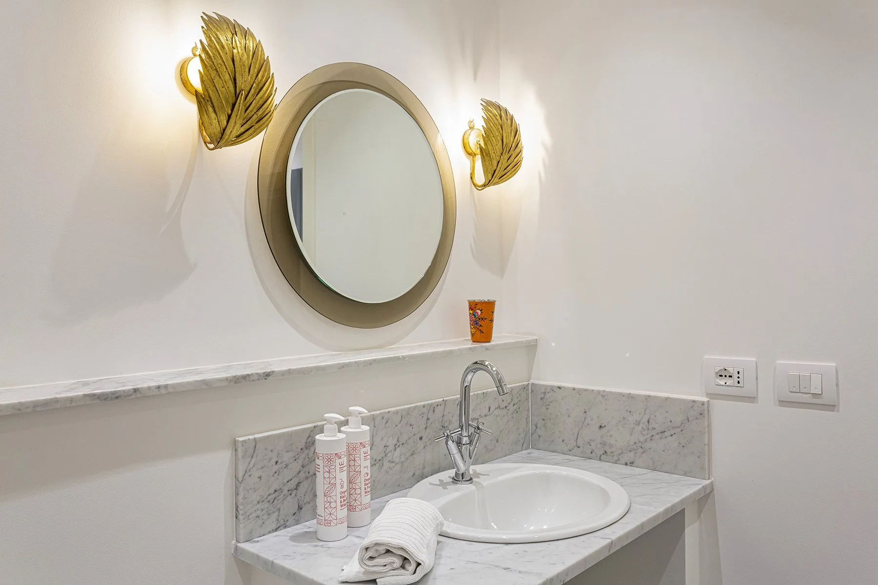 A bright bathroom vanity with a round mirror and sink.