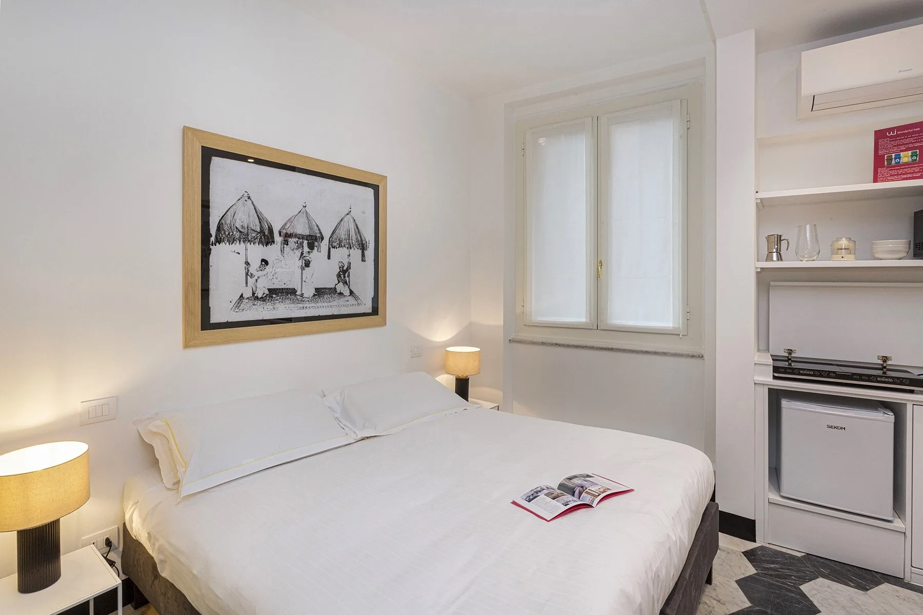 A bedroom with a neatly made bed, framed artwork, and a window.