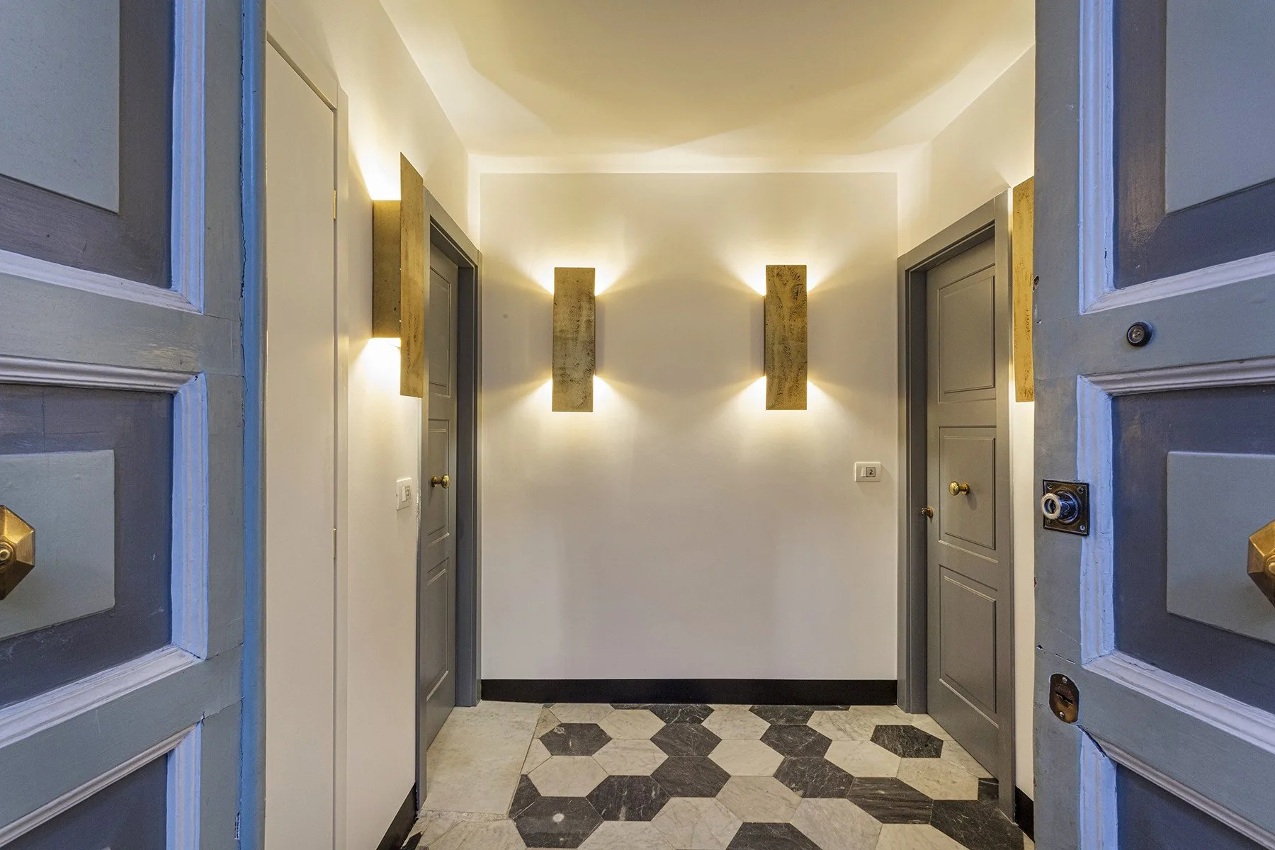 An entry hall with geometric floor tiles and wall lights.
