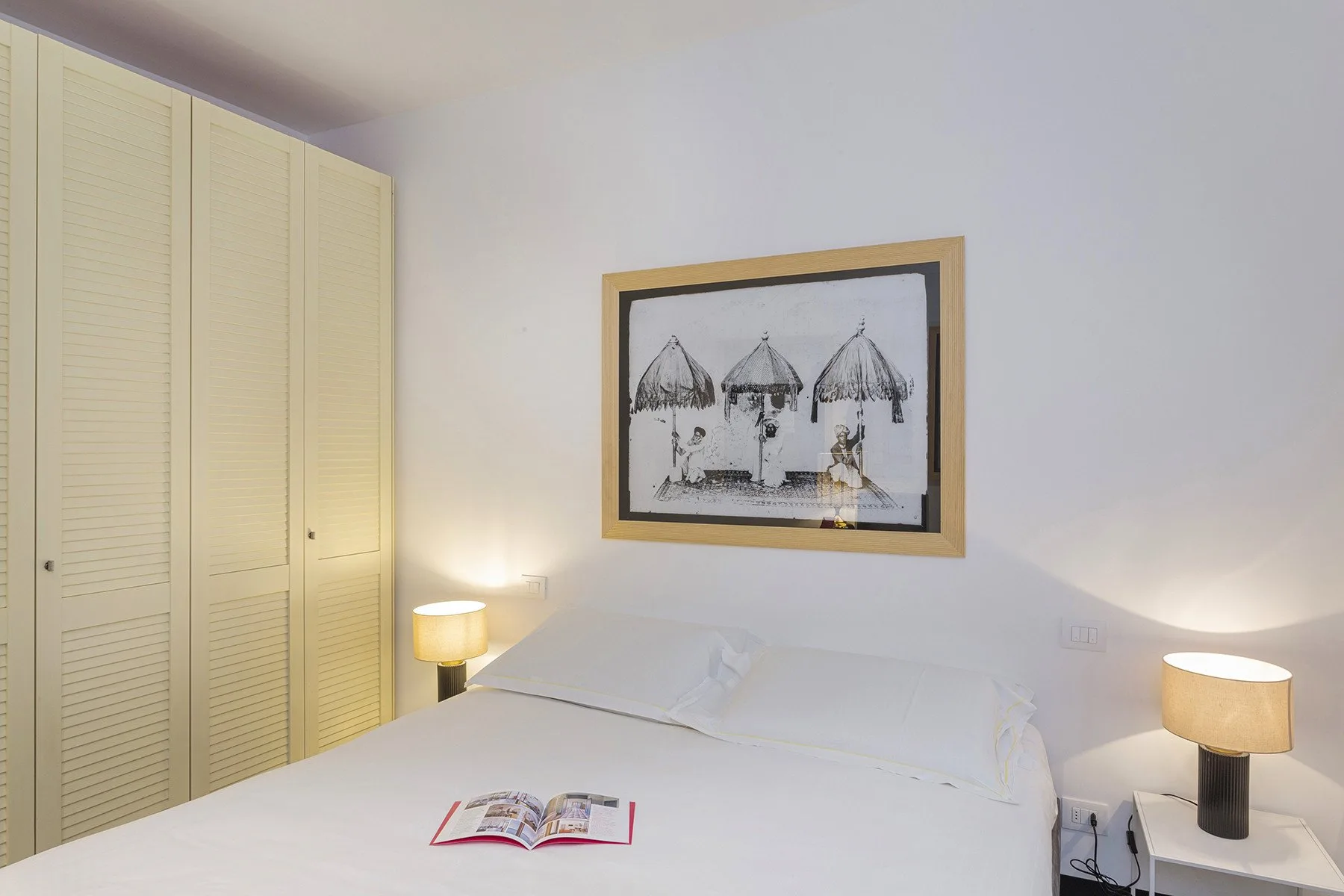 A bedroom with a bed, bedside lamps, and a framed picture on the wall.